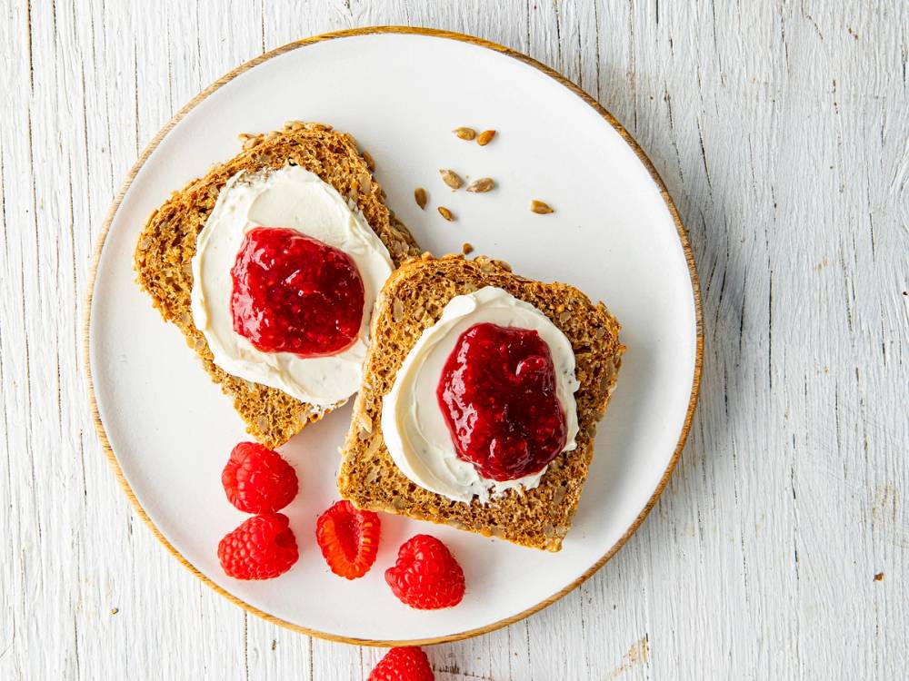 Bilde av et glass med syltetøy laget av bær, plassert på et lyst bord.
