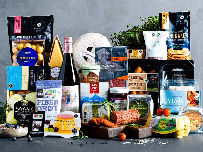 Et utvalg av matvarer og drikkevarer, inkludert ost, kjøtt, brød og grønnsaker, er plassert på en benk med en plante i bakgrunnen.