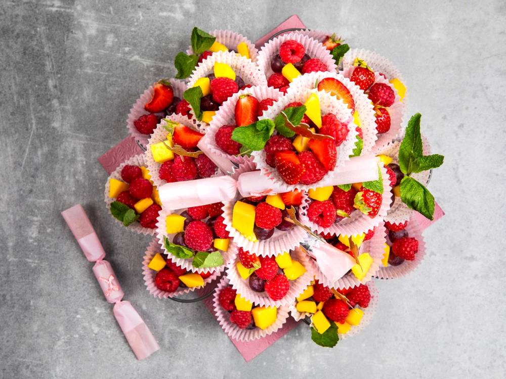 En bukett med små cupcakes dekorert med frukt og grønne blader, pakket inn i rosa papir, til en babyshower.