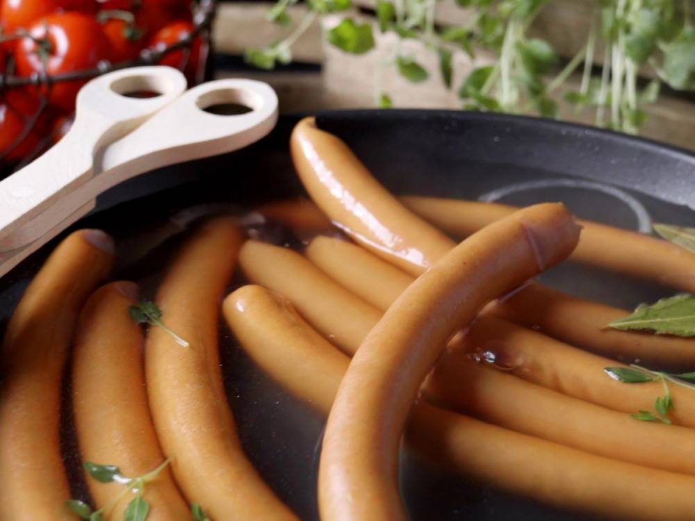 Wienerpølser stekes i en panne med noen grønne urter, sannsynligvis persille, på toppen.