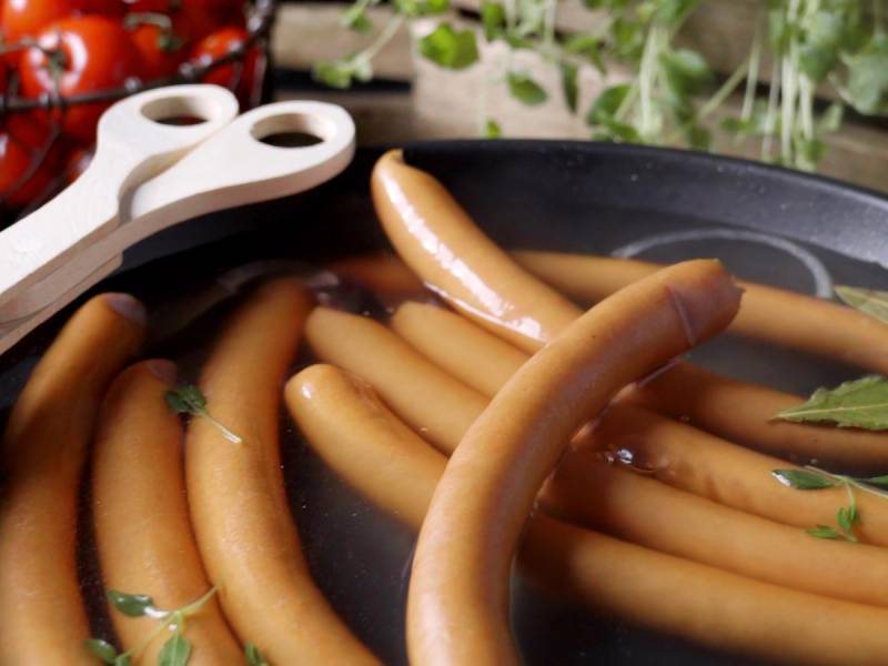 Wienerpølser stekes i en panne med noen grønne urter, sannsynligvis persille, på toppen.