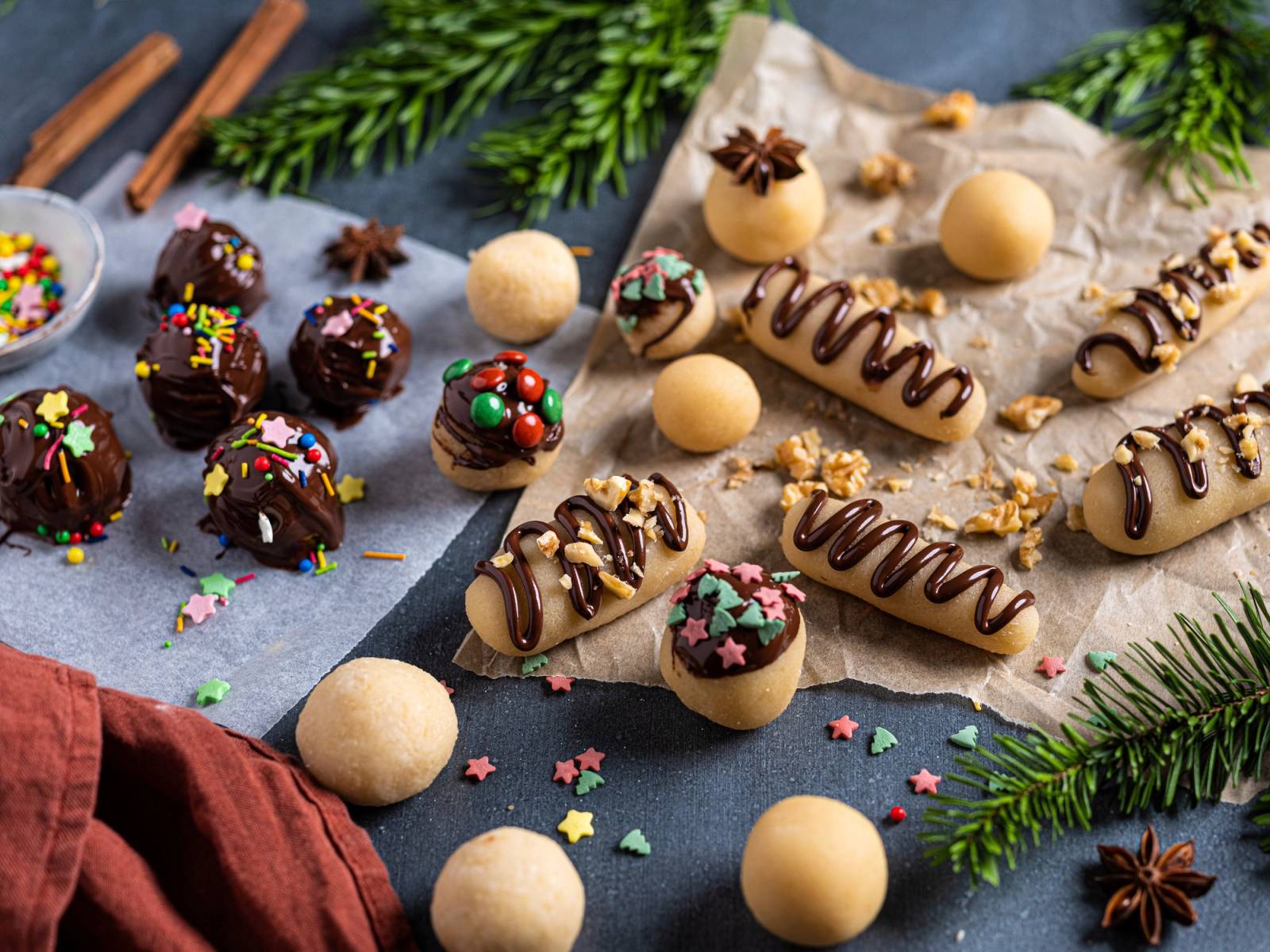 Ulike marsipankonfekt og sjokoladekaker med pynt på et bord, omgitt av granbar og stjerneanis.