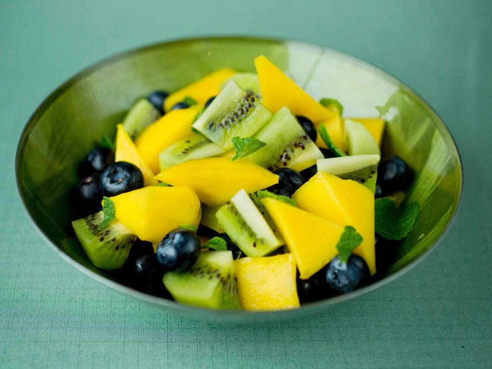 En skål med kiwi, mango og blåbær i en grønn bolle på et bord