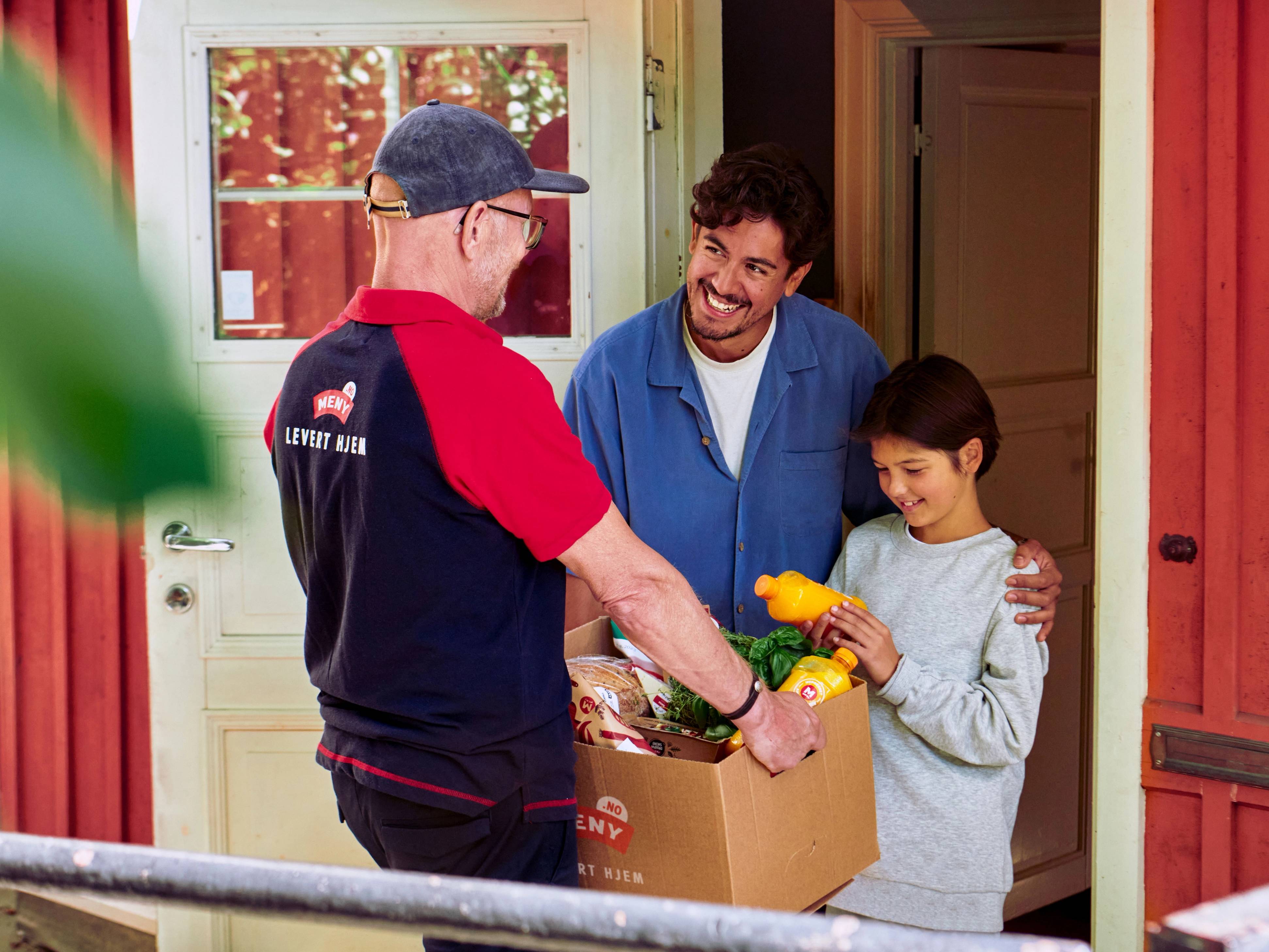 En mann i en rød og svart uniform leverer mat til en jente og en mann i et hus, med en blomsterbukett i hånden.