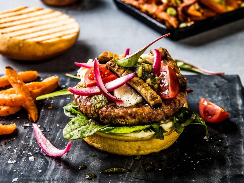 Svineburger med grottelagret taleggio ost, salat og syltede rødløk på en svart tallerken.