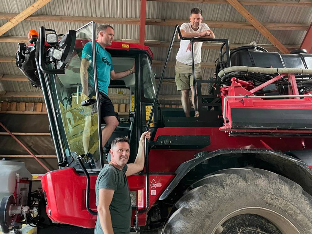 Tre menn ved en stor rød landbruksmaskin
