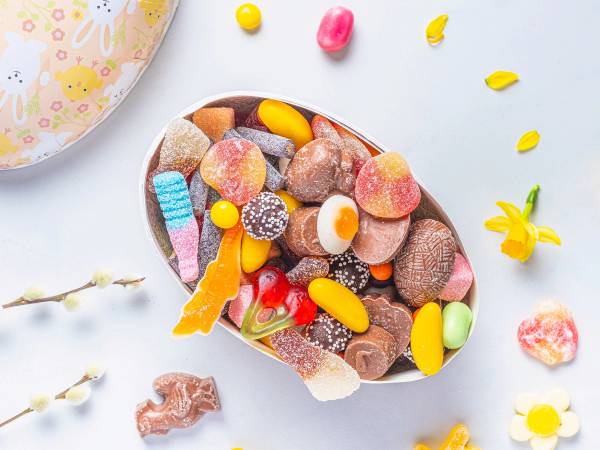 Et utvalg av smågodt i en skål med ulike farger og former, plassert på en lys bakgrunn med noen spredte godteribiter rundt.