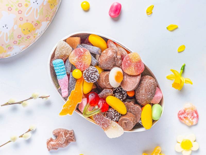 Et utvalg av smågodt i en skål med ulike farger og former, plassert på en lys bakgrunn med noen spredte godteribiter rundt.