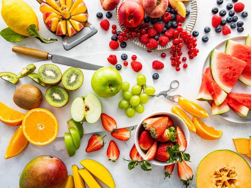 Fargerik oppskjæring av ulike frukter som vannmelon, kiwi, eple, druer og sitron på et hvitt bord.