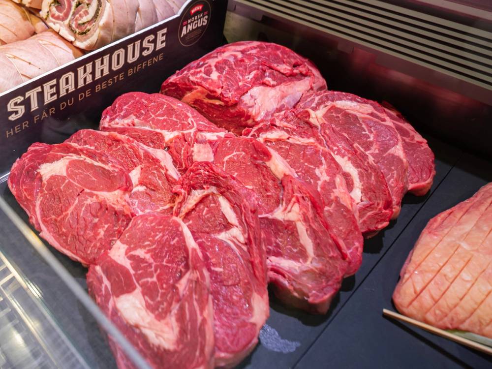 Ulike utvalg av ferske kjøttstykker på en butikkdisk, med en pakke med kjøtt i bakgrunnen.