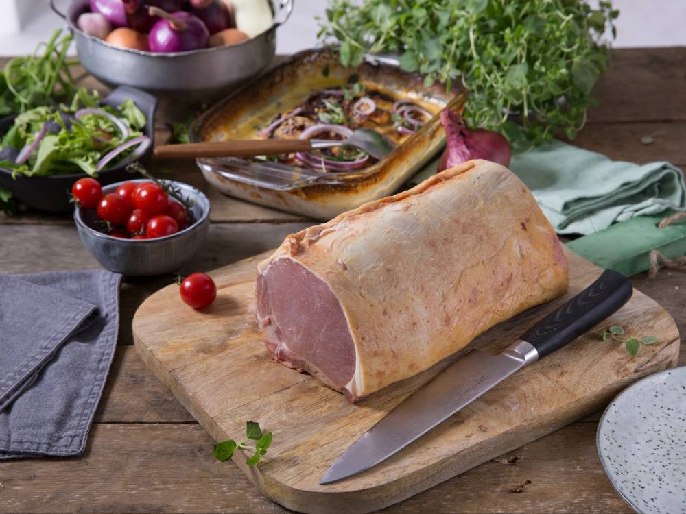 Svinekam på skjærefjøl med urter og grønnsaker rundt, klar til å bli tilberedt.