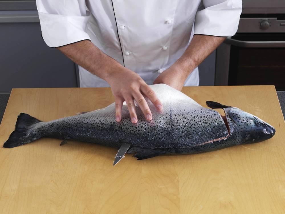 Person som fileterer en hel laks på et kjøkkenbord.
