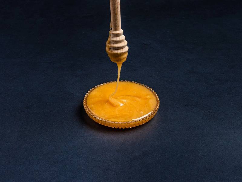 Honning som drypper fra en trepinne ned i en liten skål, sannsynligvis på en butikkhylle.