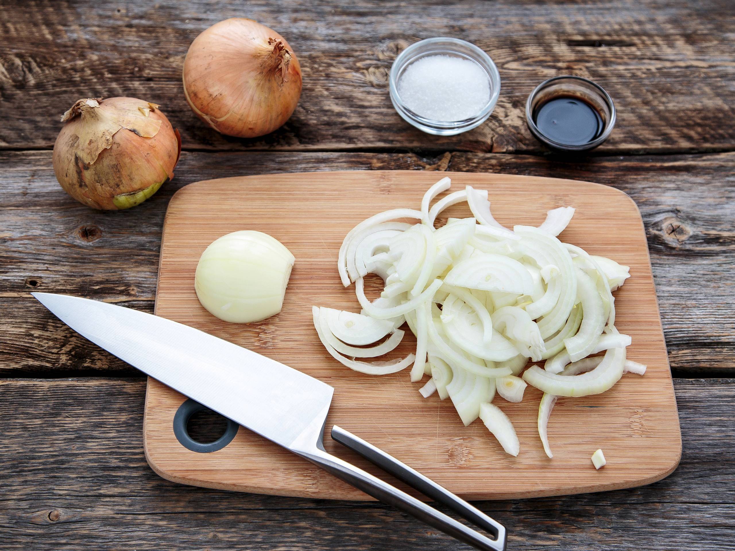 To løk, en hvit og en rød, en kniv, en liten bolle med salt og en liten bolle med soyasaus på et skjærebrett.