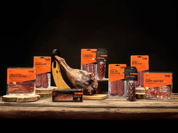 Ulike typer kjøtt og en banan på en treplate, med flere pakker med kjøtt rundt, mot en mørk bakgrunn.