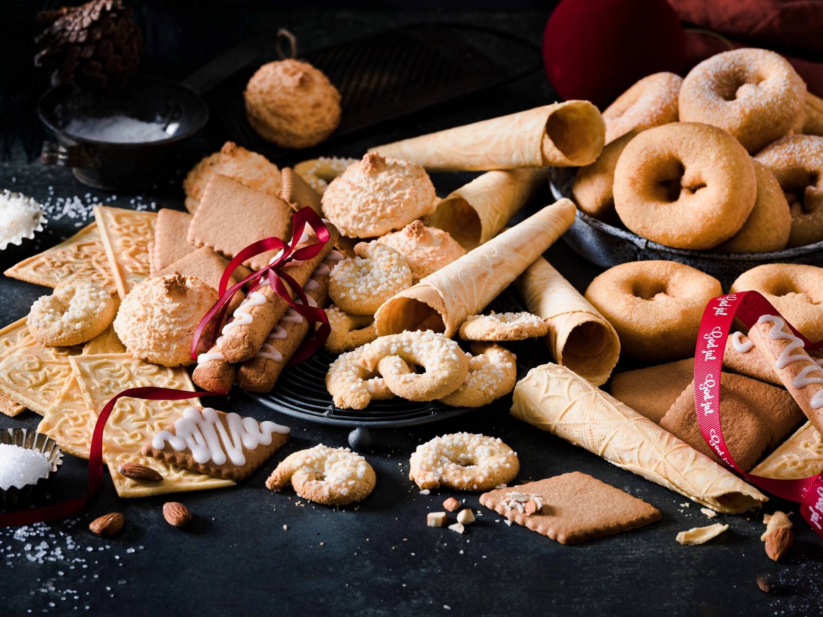 Et utvalg av julekaker og kjeks på et svart fat, med noen kjeks som er pyntet med hvitt melis og en rød sløyfe.
