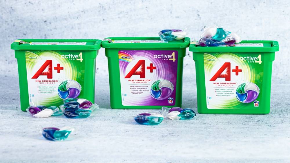 Tre grønne oppvaskmiddelbokser med blå og lilla oppvaskbørster og skum rundt på en hvit overflate.