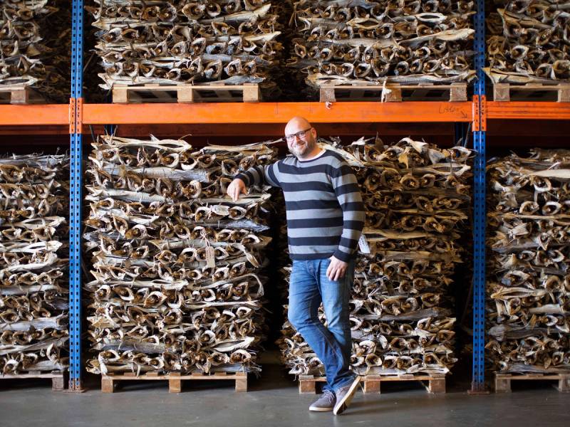 En person med en stripete genser og jeans står foran hyller med lutefisk i et lager.