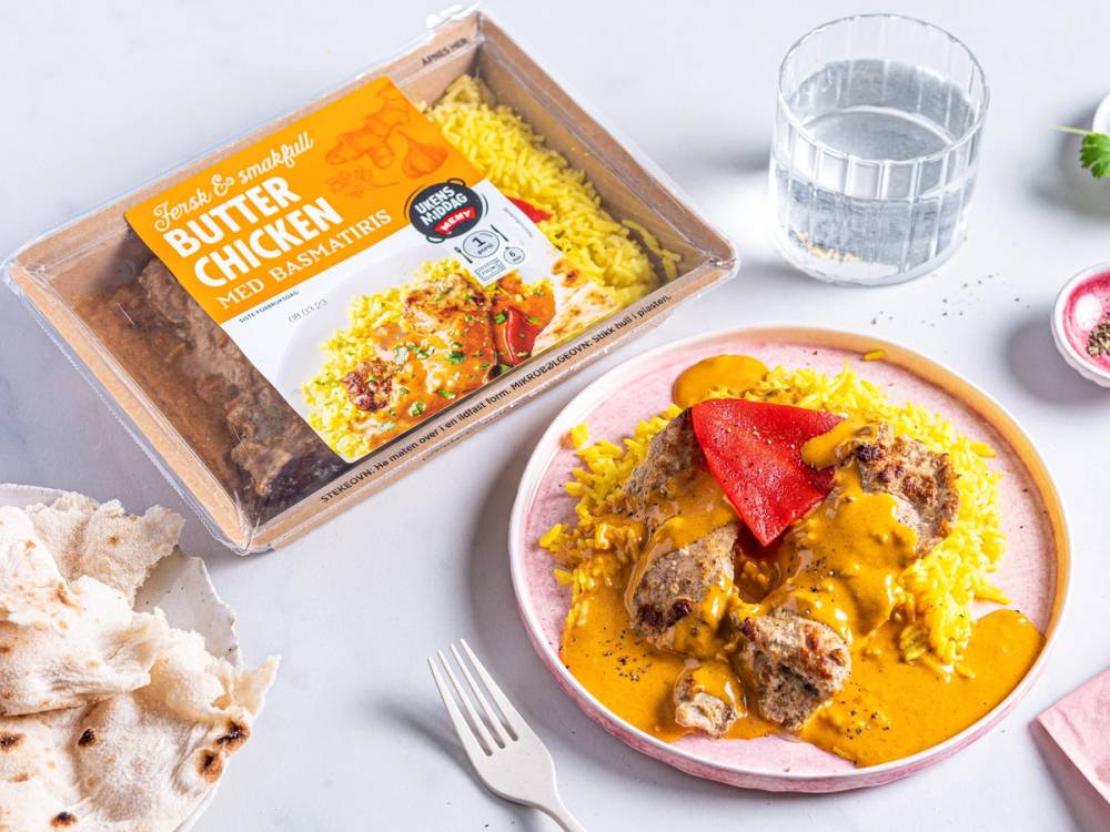 Ferdig oppvarmet takeaway-rett med kjøttboller og saus på en tallerken, med en glass vann og brød i nærheten.