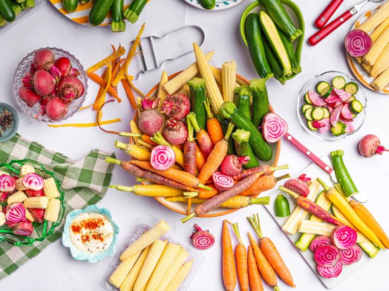 Fargerike grønnsaker og mini plakat med bilder av ulike grønnsaker på et bord.