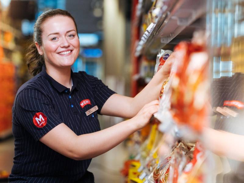 En person med bløt ansiktsmaske handler i en dagligvarebutikk, og plukker varer fra en hylle.