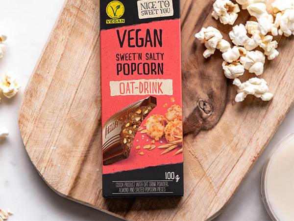 En sjokoladebar med smak av vegansk saltet popcorn og havregryn, plassert på et trebord med popcorn rundt.