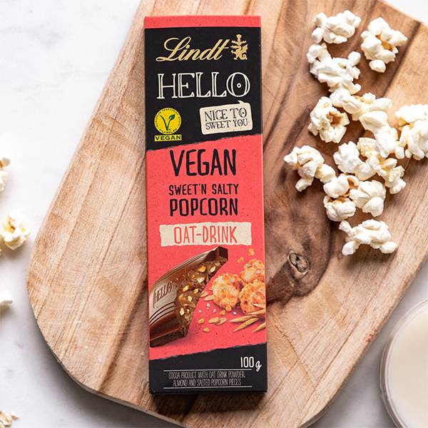 En sjokoladebar med smak av vegansk saltet popcorn og havregryn, plassert på et trebord med popcorn rundt.