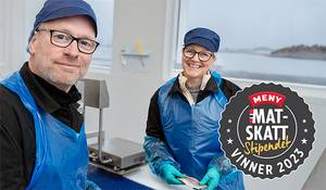 To personer i blå arbeidsklær står i et rom med utsikt over sjøen, og en logo for MatSkatt 2022 er synlig på bildet.