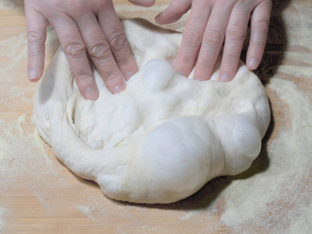 To hender former en pizzadeig til et glutennettverk på et kjøkkenbord.