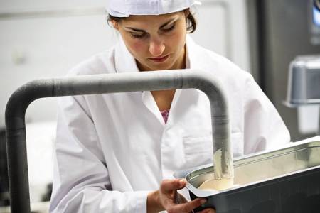 En person i hvit kokkebluse som heller røre i en stor bolle i et kjøkken, med fokus på arbeidsprosessen.