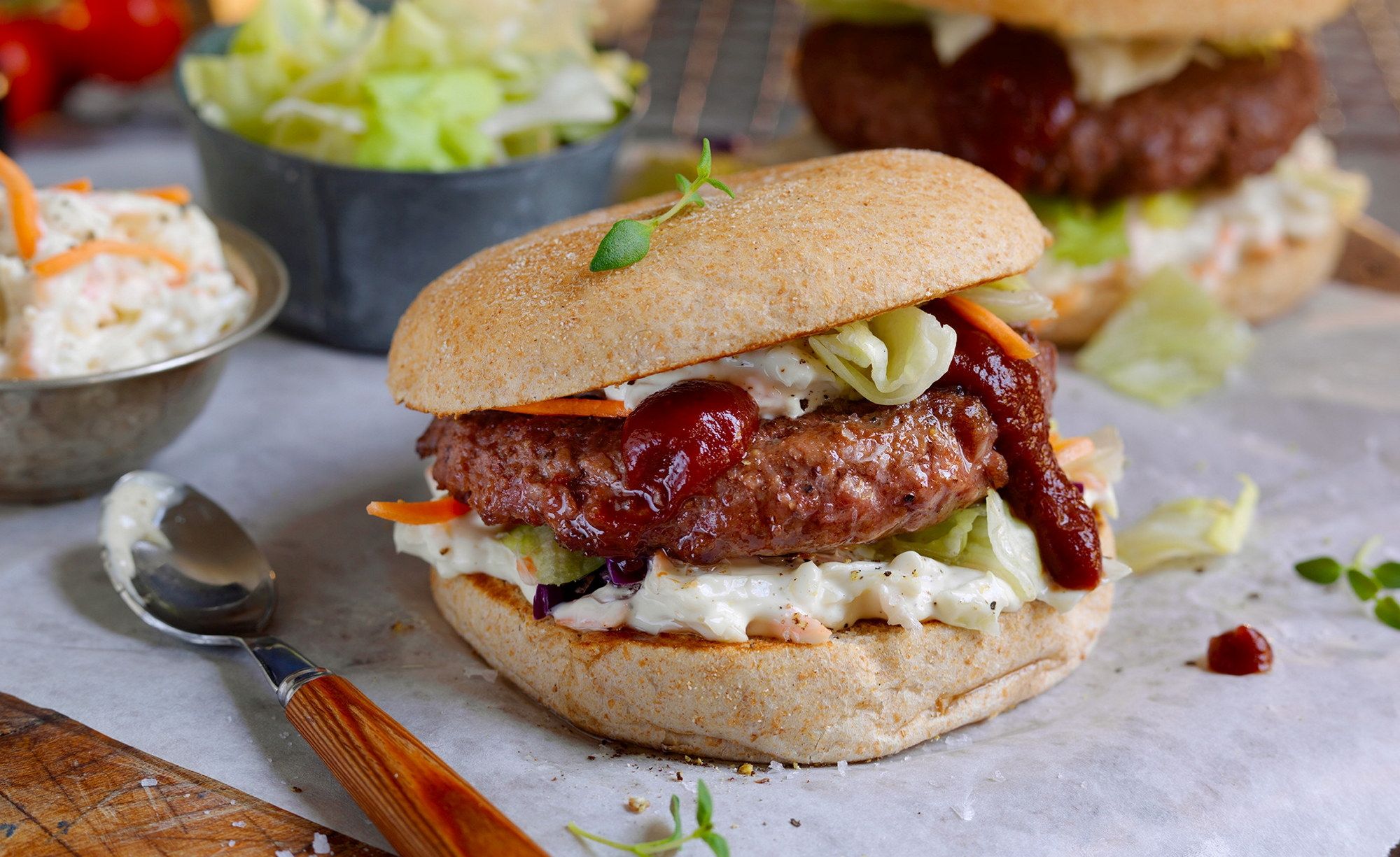 Hamburger med coleslaw og ketchup i et hamburgerbrød, med en skje med coleslaw ved siden av.