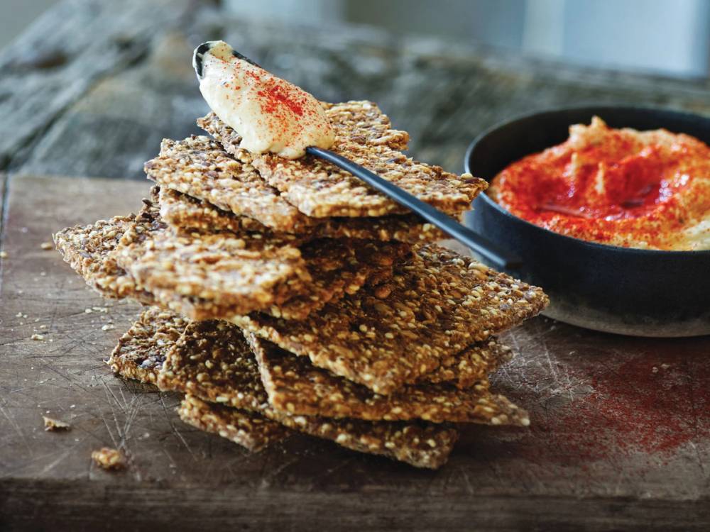 Sigdal knekkebrød stablet på et trebord med en skål med rød saus ved siden av.