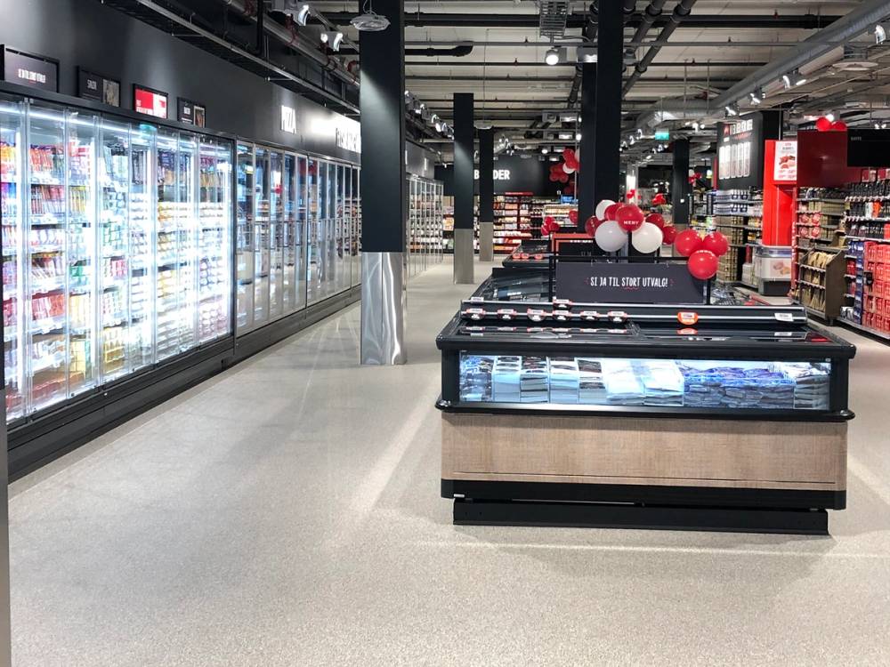 Innendørs i en dagligvarebutikk med kjøledisk og hyller fylt med varer, dekorert med røde og hvite ballonger.