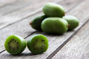 To halverte kiwibær med grønn fruktkjøtt og svarte frø, plassert på en treoverflate, med flere hele kiwibær i bakgrunnen.