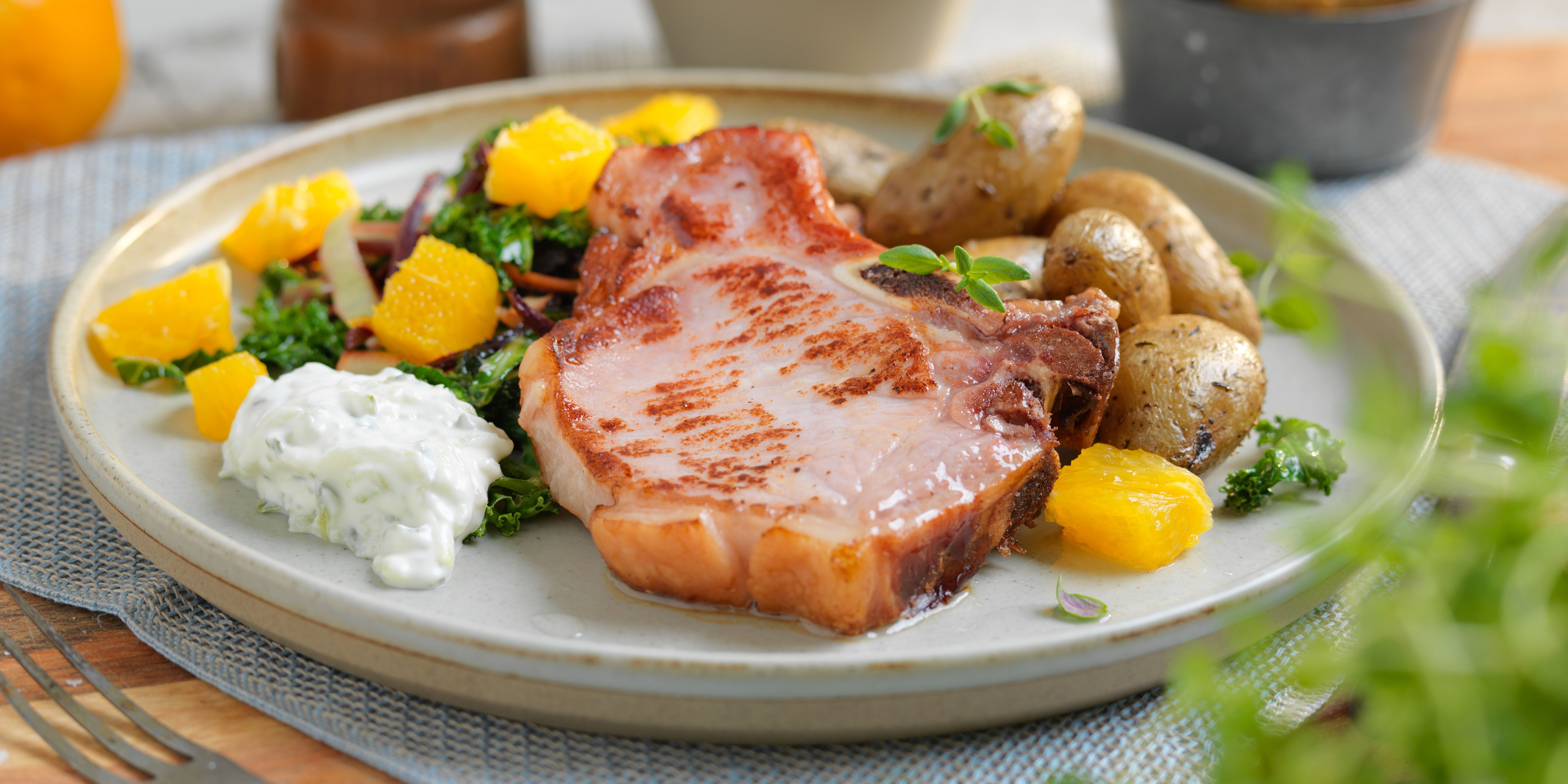 Stekt kotelett med poteter, grønnsaker og saus på en tallerken, klar for servering.