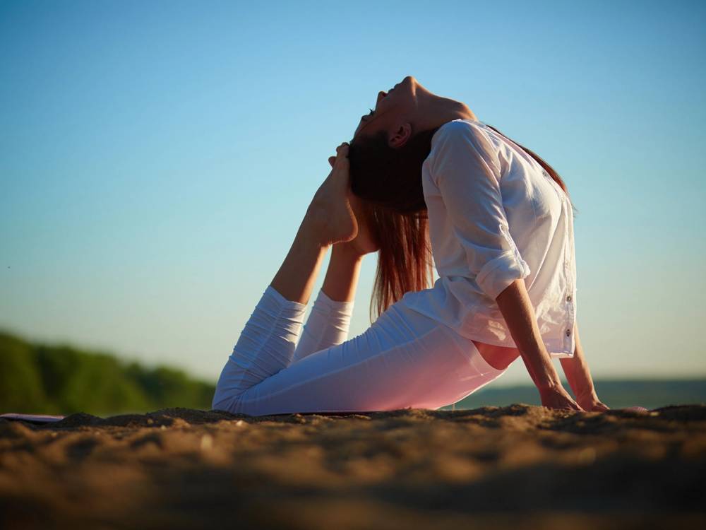 En kvinne sitter på bakken med hodet bakover og hånden i håret på en solrik dag.