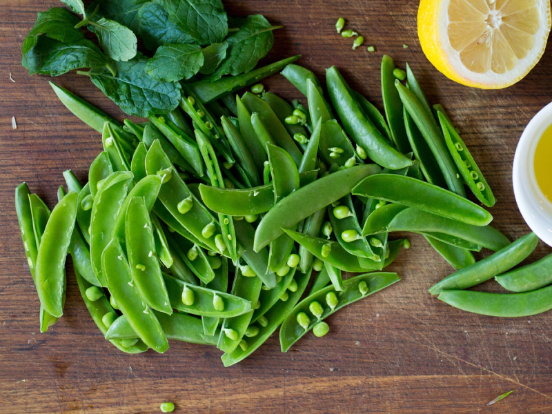 Ferske sukkererter med noen sitronbåter og en kopp med olje på et trebord