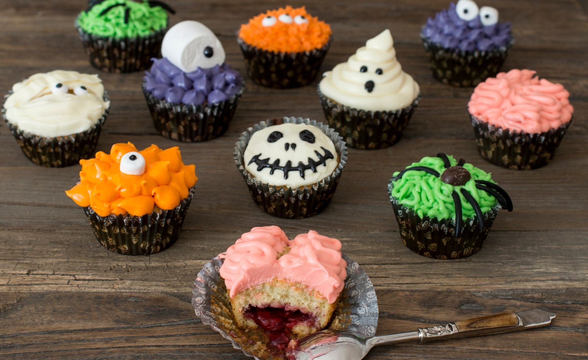 En rekke halloween-inspirerte cupcakes med ulike dekorasjoner, inkludert en med en liten skje som har tatt en bit av en cupcake.