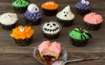 En rekke halloween-inspirerte cupcakes med ulike dekorasjoner, inkludert en med en liten skje som har tatt en bit av en cupcake.