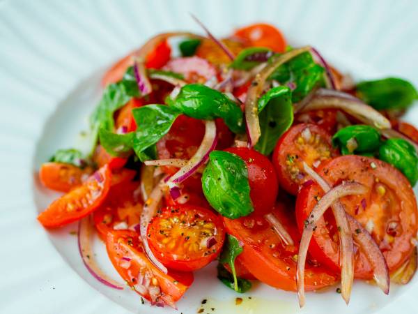 En frisk og enkel salat med cherrytomater, rødløk og grønn basilikum på en hvit tallerken