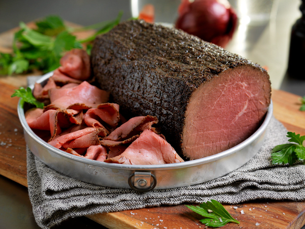 Roastbiff med skiver av rosa kjøtt og grønt tilbehør på en tallerken.