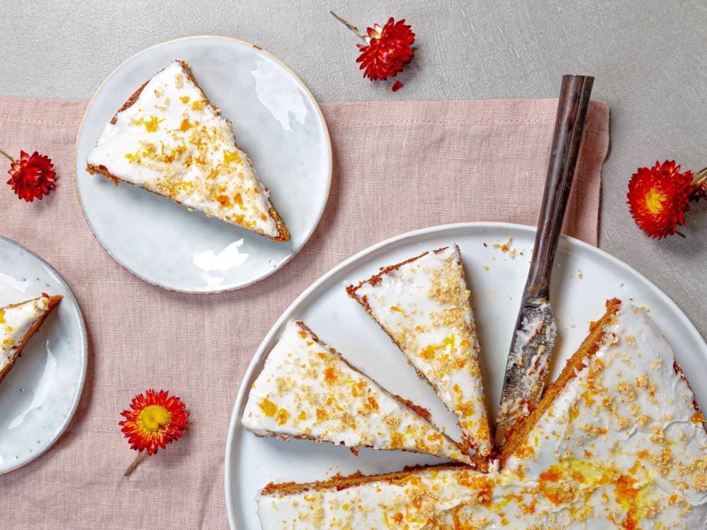 Gulrotkake med kremostfyll og pyntet med revet gulrot, delt opp på et fat med noen enkeltstykker på små tallerkener.