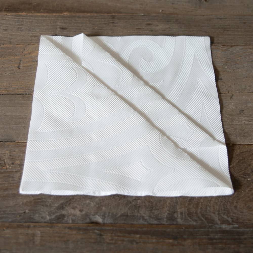 En hvit juleserviett med dekorative mønstre ligger brettet på en treoverflate.