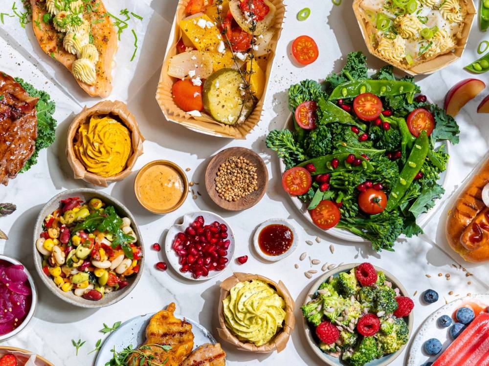 Et utvalg av ulike retter og salater på et bord, inkludert en grønn salat med cherrytomater, en bolle med kyllingsalat, og flere små tallerkener med dressinger og tilbehør.