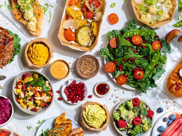 Et utvalg av ulike retter og salater på et bord, inkludert en grønn salat med cherrytomater, en bolle med kyllingsalat, og flere små tallerkener med dressinger og tilbehør.