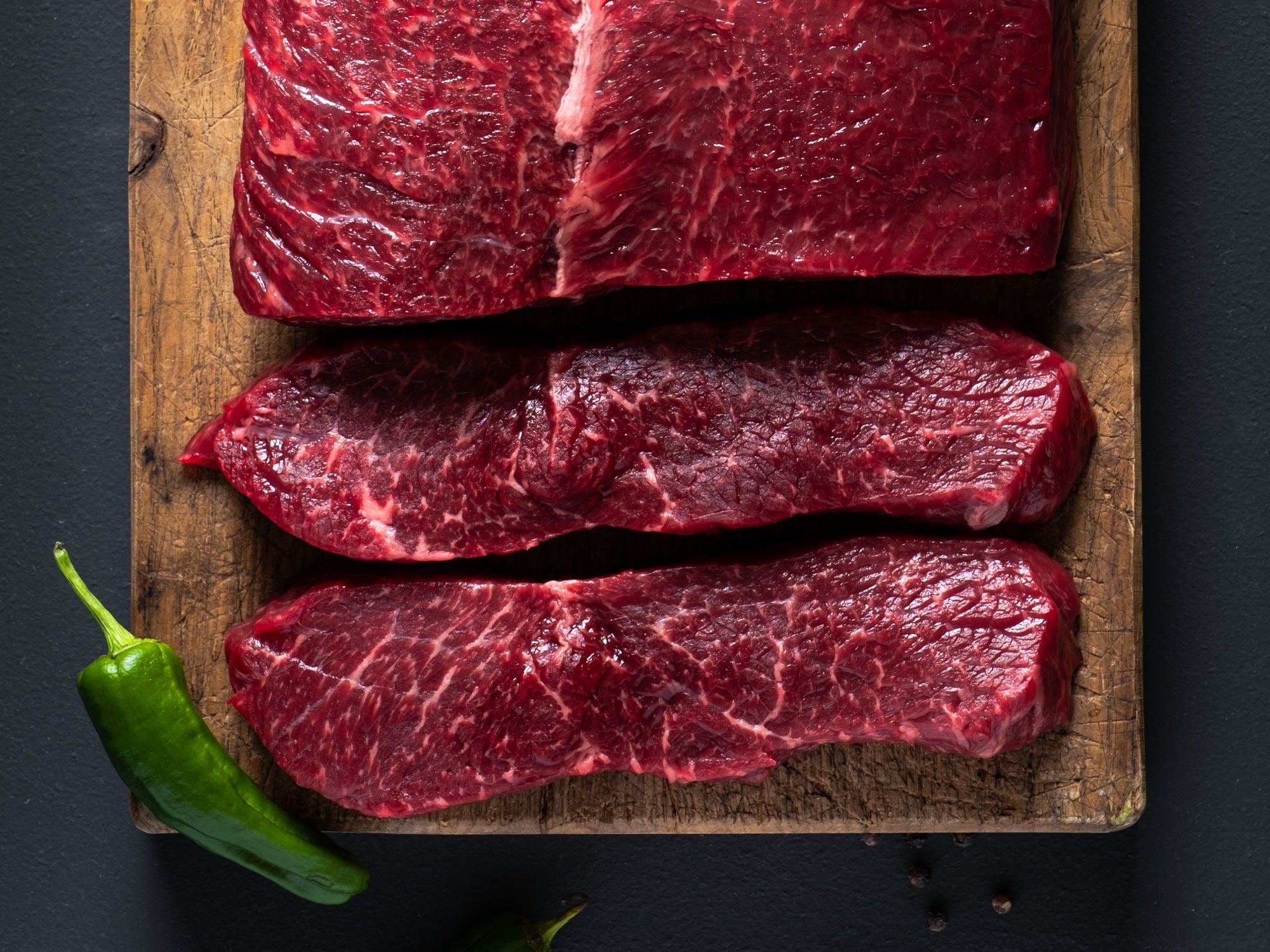 Tre stykker angus ytrefilet på en skjærefjøl med en grønn chili i hjørnet.