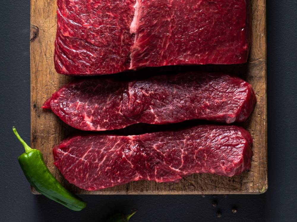 Tre stykker angus ytrefilet på en skjærefjøl med en grønn chili i hjørnet.