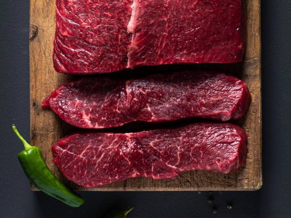 Tre stykker angus ytrefilet på en skjærefjøl med en grønn chili i hjørnet.