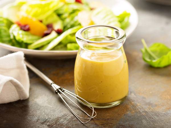 En glasskrukke med vinaigrettesaus står på et bord med en salat i bakgrunnen.