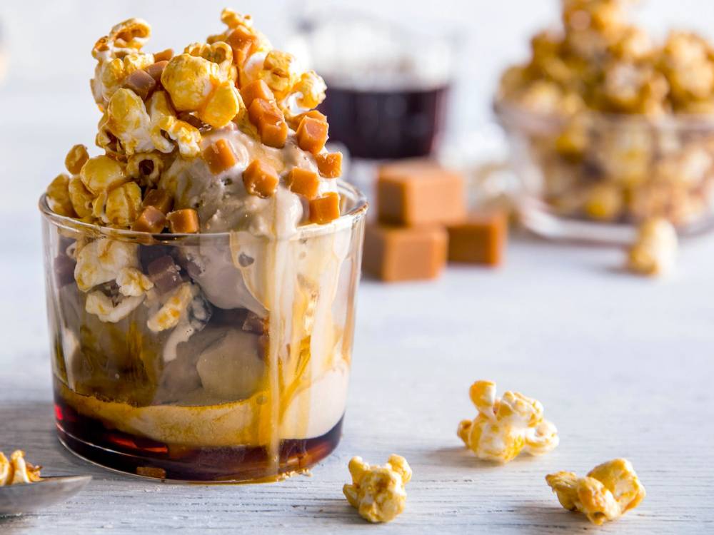 Karamellisert popcorn og fudge i et glass, med flere fudgebiter i bakgrunnen.